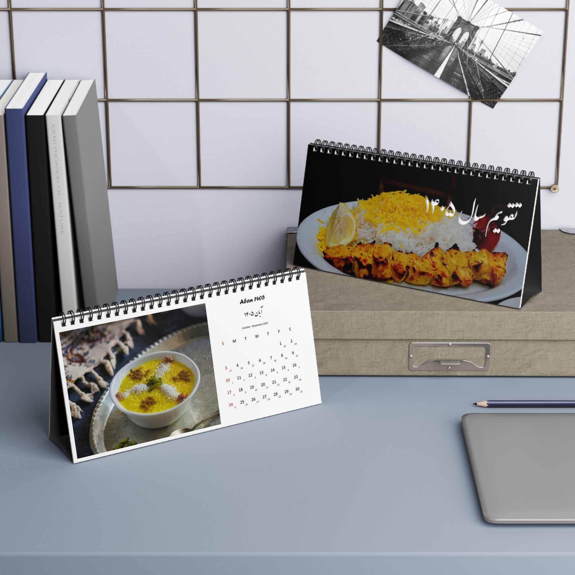Two calendars with persian iranian food images on a desk against a tiled wall.